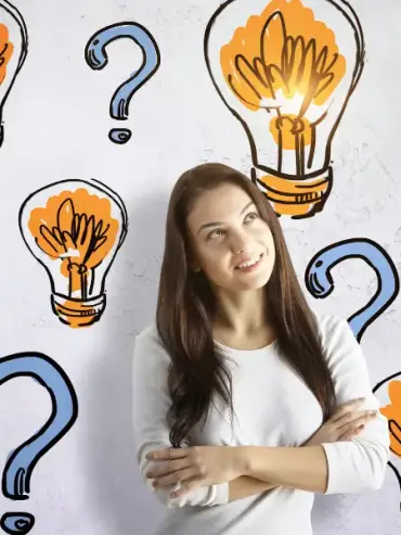 A woman with long brown hair stands smiling with arms folded in front of a wall decorated with drawn light bulbs and question marks, suggesting she has an idea for hot tub repair or is thinking creatively about service solutions.