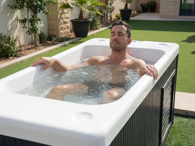 TubLease Hot Tub Rental and Sales 3 A man with short dark hair relaxes with his eyes closed whilst sitting in a modern outdoor bath filled with water, enjoying recovery surrounded by green grass and potted plants—an oasis that feels straight out of Dubai.
